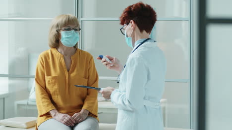 Doctor-in-Mask-Measuring-Temperature-of-Elderly-Woman-in-Clinic